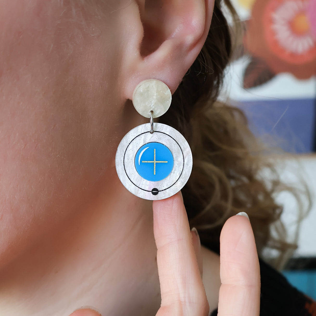 Hydrogen atom dangle earrings made from laser cut acrylic. being modelled.