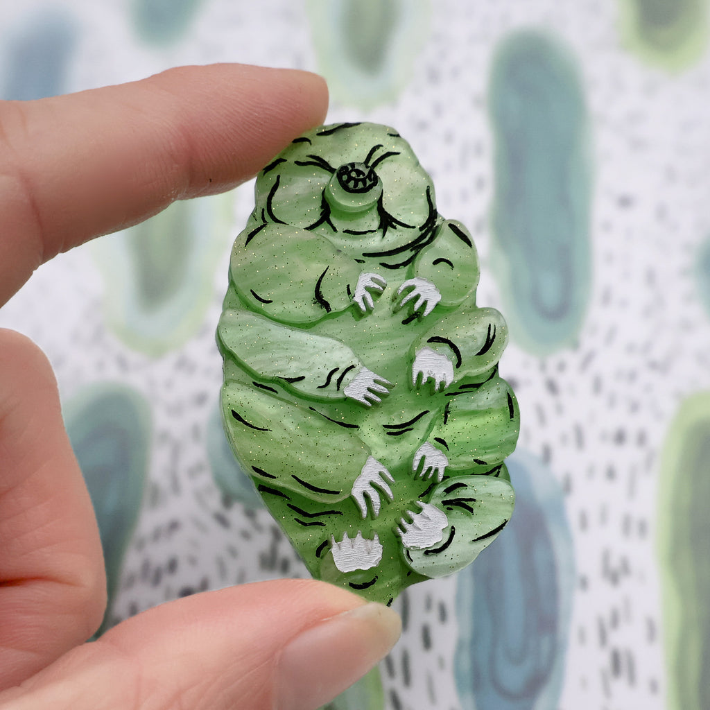 Closeup of green acrylic tardigrade brooch held between fingers