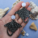 Laser cut arylic eagle spotted ray dangle earrings being held in palm.