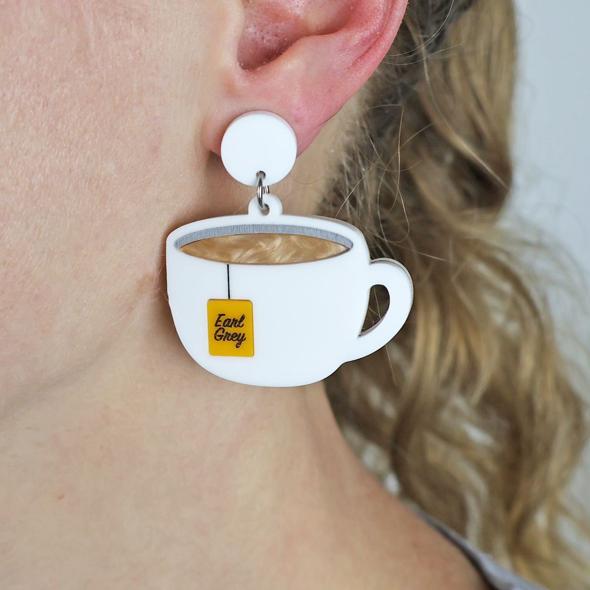 White teacup earrings with an Earl Grey teabag label worn by a person