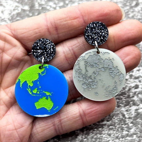 Asymmetrical acrylic earth and moon earrings, hanging from black glitter acrylic toppers.