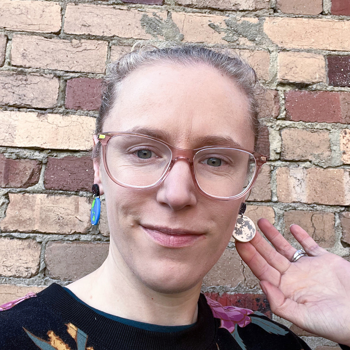 Asymmetrical earth and moon earrings being modelled by the maker, a blonde woman with glasses.