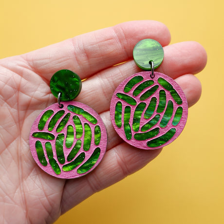 Pink and green earrings held in a hand, depicting an e.coli colony.