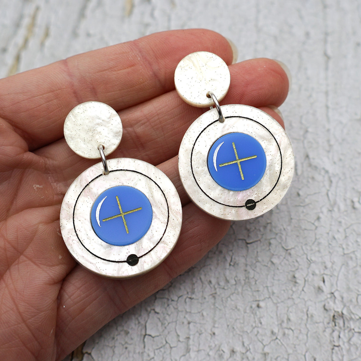 Hydrogen atom dangle earrings made from laser cut acrylic. Being held up to the camera. 