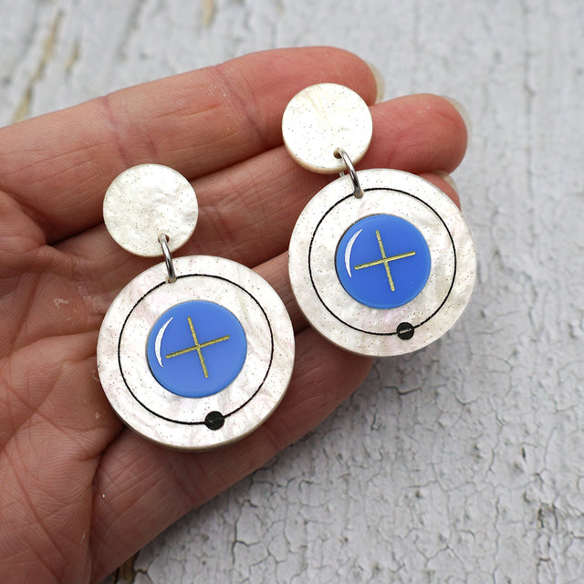 Hydrogen atom dangle earrings made from laser cut acrylic. Being held up to the camera. 