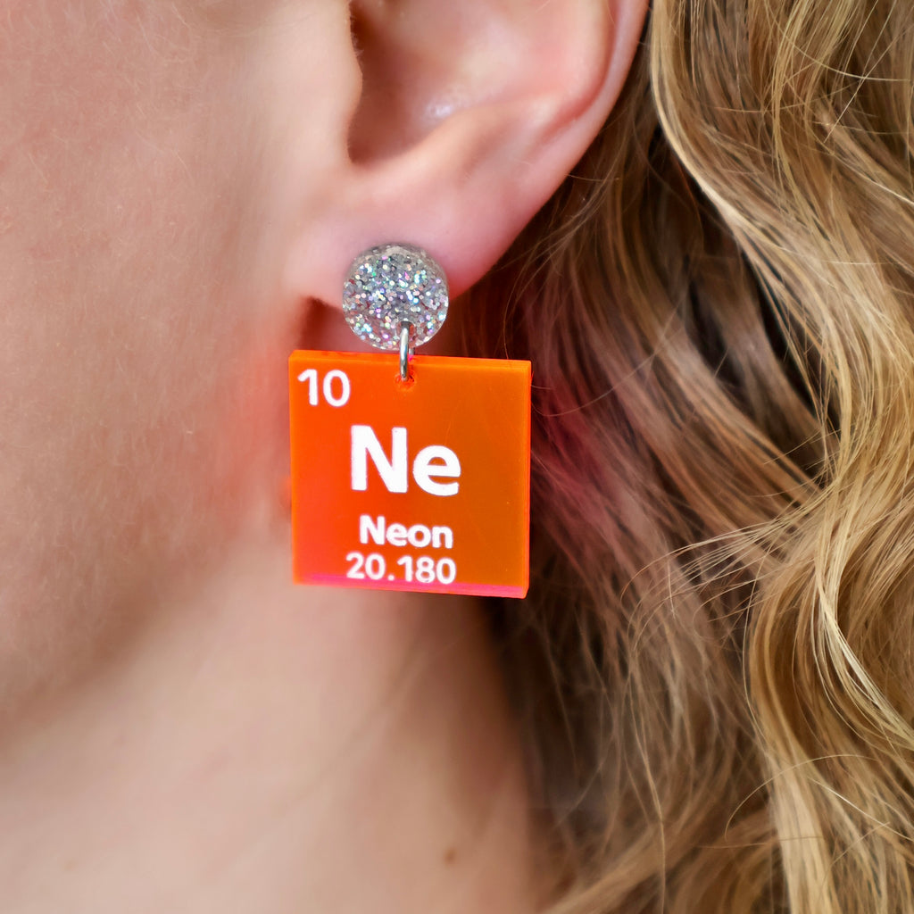Neon periodic table earrings in neon pink acrylic and glittery silver earring toppers, being modelled. 