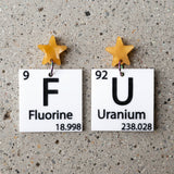 black and white asymmetrical periodic table earrings with 'Fluorine' and 'Uranium' labels, and yellow star toppers. 