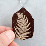 Acrylic fern leaf pendant necklace held by a hand