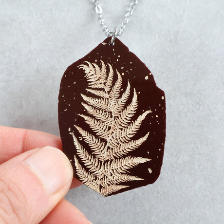Acrylic fern leaf pendant necklace held by a hand
