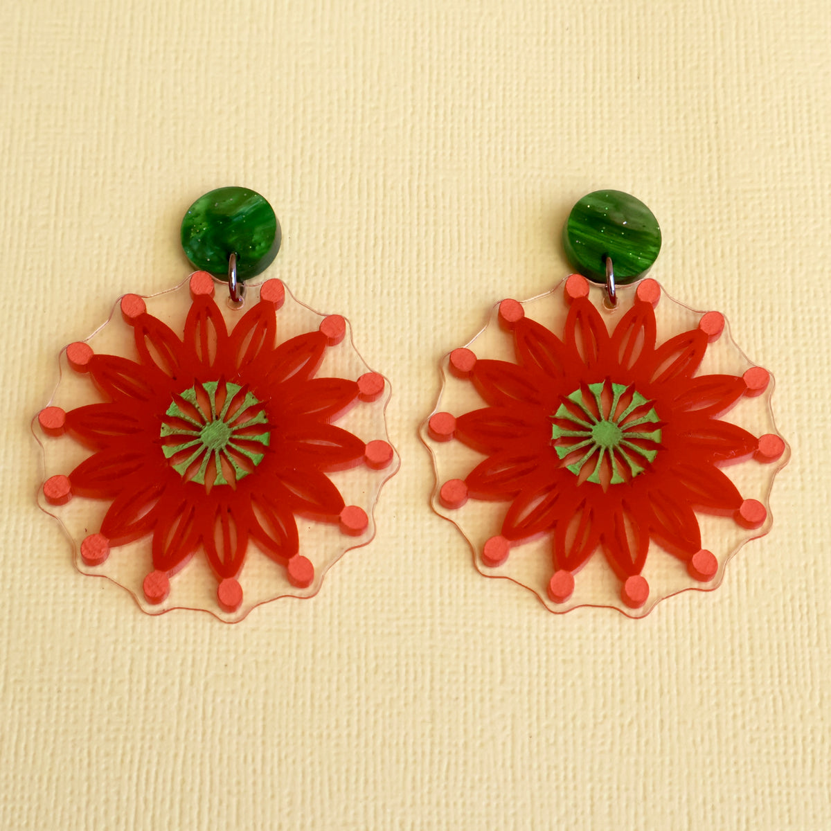 Acrylic Firewheel tree earrings closeup. Earrings are red with green round acrylic toppers. 