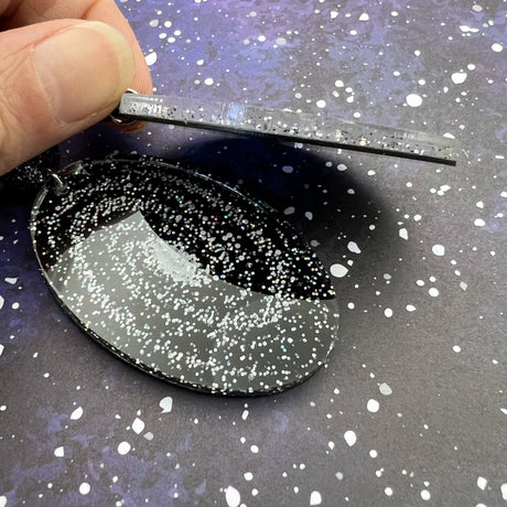 Side view of a pair of statement sized milky way galaxy earrings, oval in shape and laser cut in glittery acrylic. 