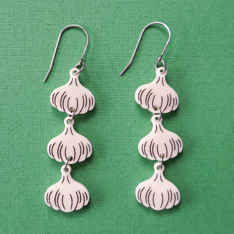 Close-up photo of a pair of garlic earrings. 3 garlic bulbs dangle from each French hook. 
