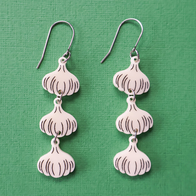 Close-up photo of a pair of garlic earrings. 3 garlic bulbs dangle from each French hook. 