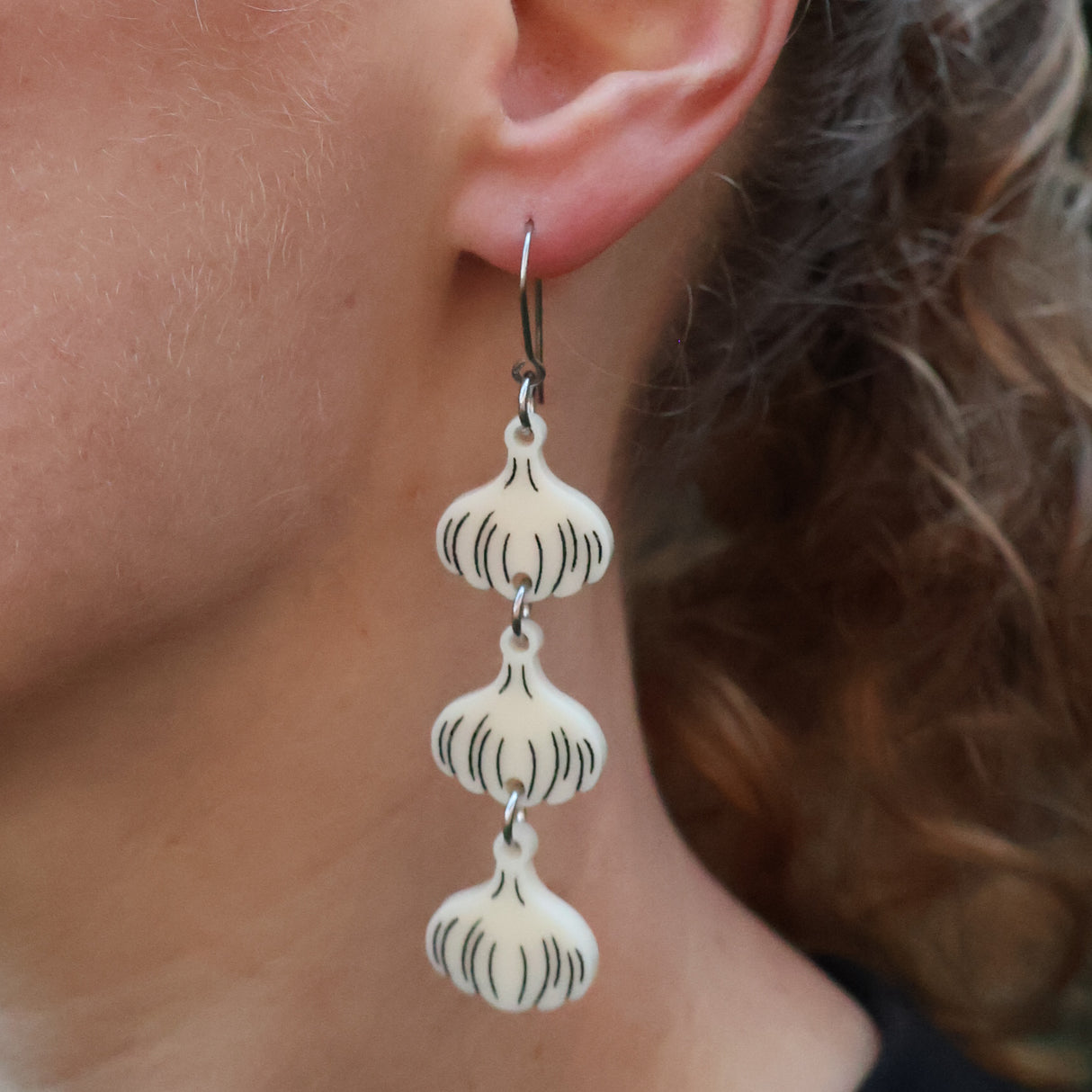 Close-up of a person wearing a pair of garlic bulb earrings, hanging from french hooks. 