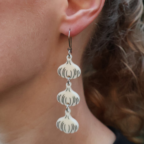 Close-up of a person wearing a pair of garlic bulb earrings, hanging from french hooks. 