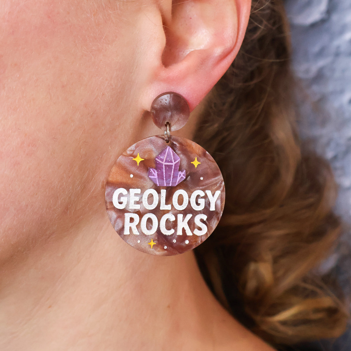 Earring with 'GEOLOGY ROCKS' text worn by a person