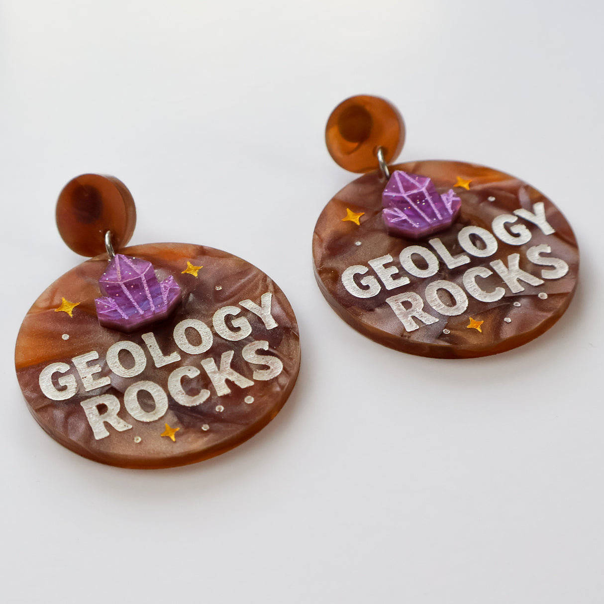 Earrings with 'Geology Rocks' text and gemstone designs on a white background
