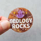 Round badge or brooch with 'Geology Rocks' text and crystal illustration held by a hand