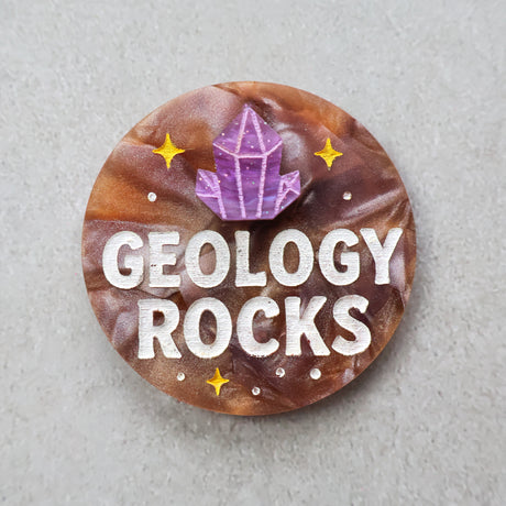 Acrylic brooch with 'Geology Rocks' text and a purple crystal design