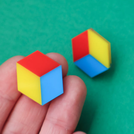 Colorful cube-shaped stud earrings in red blue and yellow tones being held in a hand.