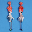 Squid-shaped acrylic earrings with red tops and pink bodies on a blue background