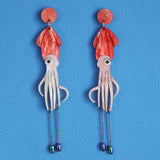 Squid-shaped acrylic earrings with red tops and pink bodies on a blue background