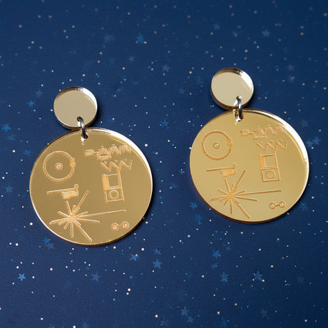 Gold toned mirror acrylic earrings with engraved designs of the voyager golden record. 
