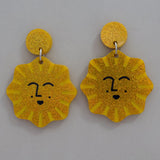 Yellow sun-shaped earrings with smiling faces on a gray background