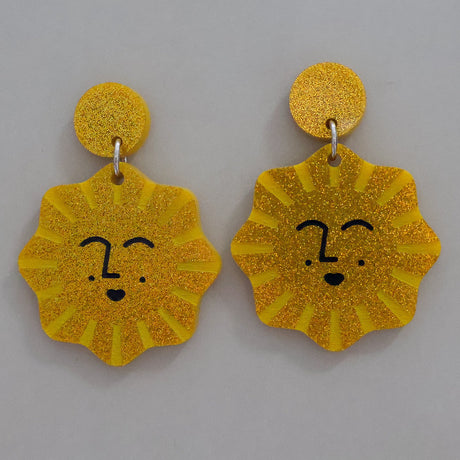 Yellow sun-shaped earrings with smiling faces on a gray background
