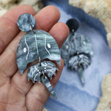 Laser cut acrylic horseshoe crab earrings. Held in hand.