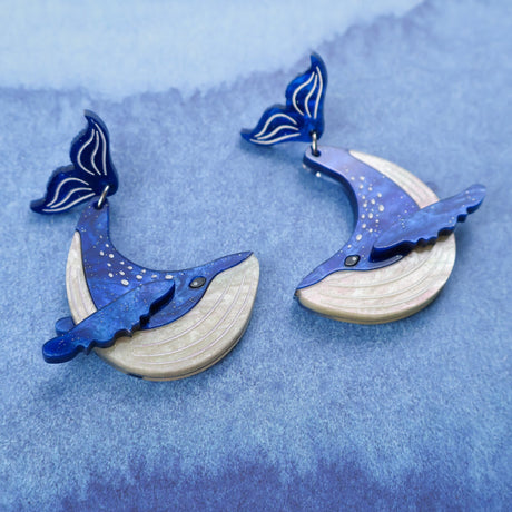 Laser cut acrylic blue humpback whale earrings closeup view. The whales tails are the earring toppers. 