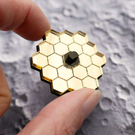 JWST mini acrylic laser cut brooch brooch being held for scale, showing gold mirror acrylic, against a moonscape background.