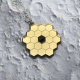 Closeup of JWST (James Webb Space telescope) pendant against a lunar backdrop, showing gold mirror acyrlic and stainless steel chain. 