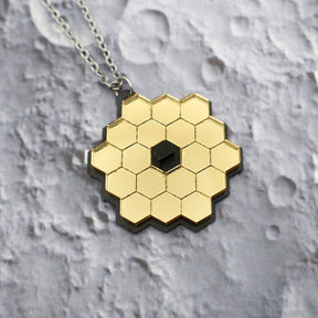 Closeup of JWST (James Webb Space telescope) pendant against a lunar backdrop, showing gold mirror acyrlic and stainless steel chain. 