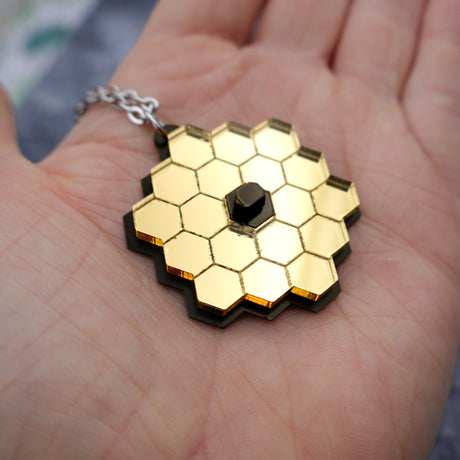 JWST (James webb space telescope) pendant in palm for scale, showing gold mirror acrylic and stainless steel chain. 