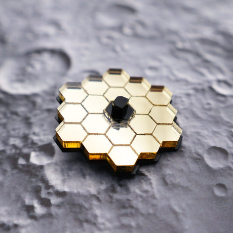 Closeup of JWST (James webb space telescope) mini brooch against a lunar backdrop
