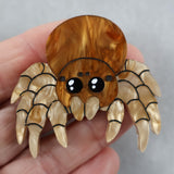 Spider-shaped acrylic brooch held in a hand against a neutral background