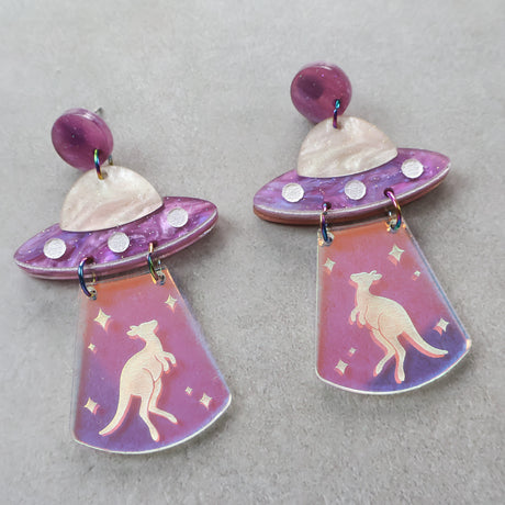 Pair of purple toned earrings with UFO design and kangaroo being abducted via a tractor beam. 