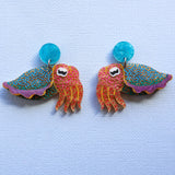 A pair of laser cut acrylic cuttlefish earrings with blue acrylic toppers, sitting against a light blue backdrop