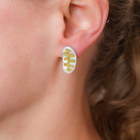 Close-up of an ear wearing a gold and light blue mitochondria stud earring.