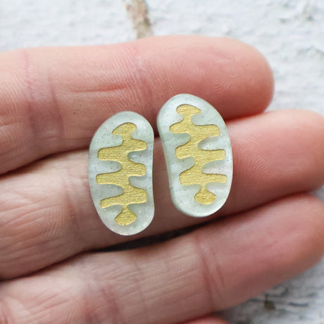 Gold and silver stud earrings shaped like mitochondria held between fingers on a light background