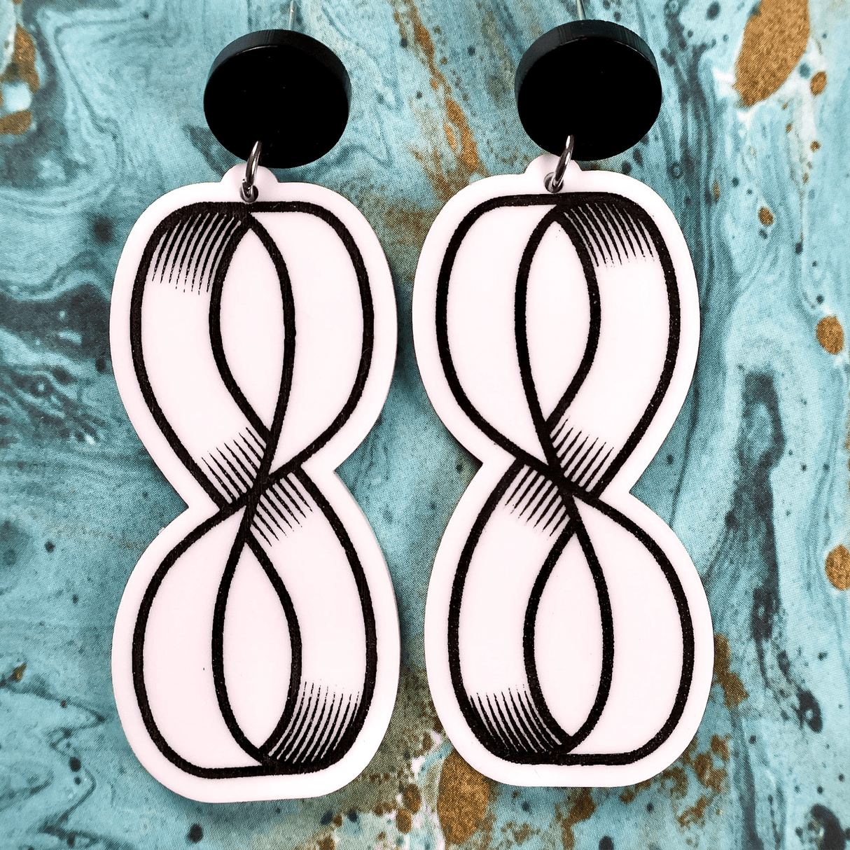 Pair of black white dangle acrylic earrings with mobius strip design on a textured blue background