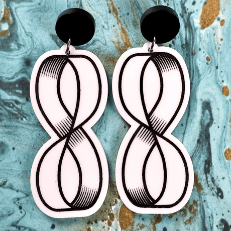 Pair of black white dangle acrylic earrings with mobius strip design on a textured blue background