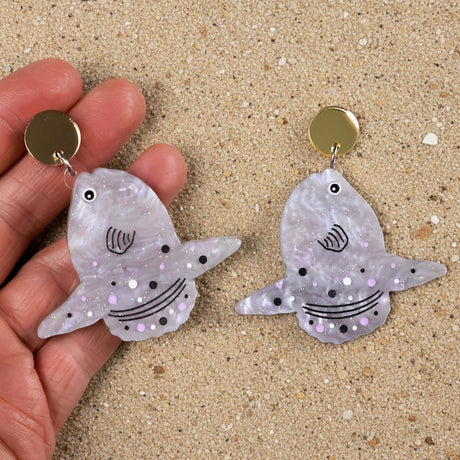 mola mula (sunfish)  earrings with glittery finish held by a hand and with gold mirror acrylic toppers. 
