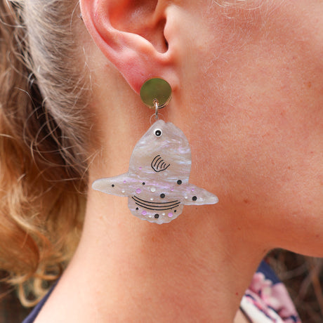 Close-up of a person wearing a sunfish earrings hanging from a gold mirror acrylic topper. 