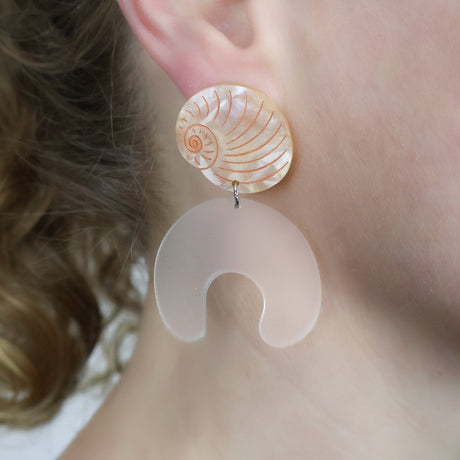 Moon snail shell and egg acrylic laser cut earrings. Being modelled.