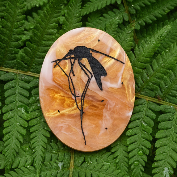 Decorative oval acrylic brooch with a black mosquito design etched into an amber looking acrylic. 