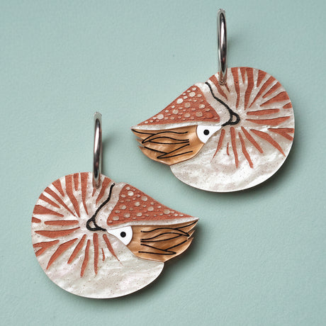 Pair of acrylic earrings with a nautilus design, hanging from huggie hoops. 