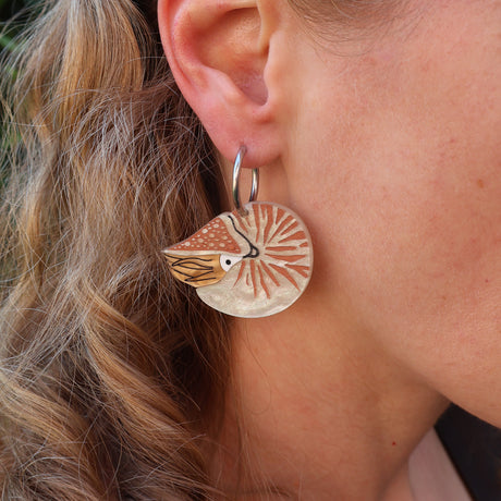 Close-up of a person wearing an acrylic nautilus earring with huggie hoop topper. 