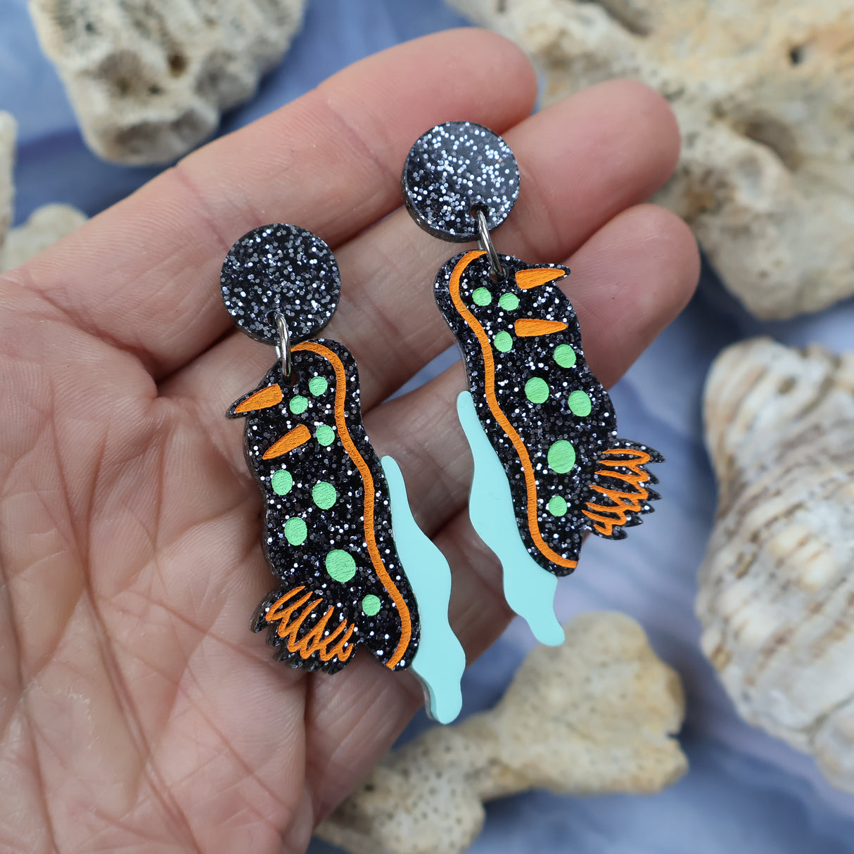 Laser cut acrylic nudibranch earrings, held in hand.